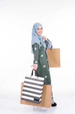 Geleneksel Asya elbisesi içinde güzel ve heyecanlı bir Müslüman kadın model beyaz arka planda izole edilmiş alışveriş torbaları taşıyor. Eidul Fitri moda ve festival hazırlık alışveriş konsepti