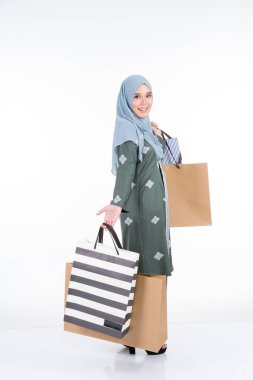 Geleneksel Asya elbisesi içinde güzel ve heyecanlı bir Müslüman kadın model beyaz arka planda izole edilmiş alışveriş torbaları taşıyor. Eidul Fitri moda ve festival hazırlık alışveriş konsepti