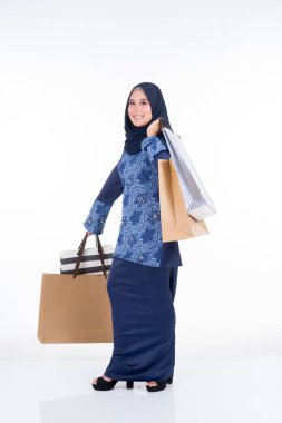 Geleneksel Asya elbisesi içinde güzel ve heyecanlı bir kadın model beyaz arka planda izole edilmiş alışveriş torbaları taşıyan modern bir kurung. Eidul Fitri moda ve festival hazırlık alışveriş konsepti