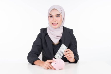 Finans ve muhasebe tasarruf kavramı. İş dünyasından Müslüman bir kadın beyaz arka planda izole bir şekilde kumbaraya bir banknot yerleştiriyor..