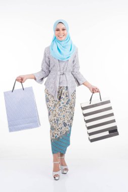 Geleneksel Asya elbisesi içinde güzel bir Müslüman kadın model modern kebaya ve beyaz arka planda izole edilmiş alışveriş torbaları taşıyan bir tesettür. Eidul Fitri moda ve festival alışveriş konsepti