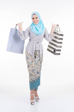 Geleneksel Asya elbisesi içinde güzel bir Müslüman kadın model modern kebaya ve beyaz arka planda izole edilmiş alışveriş torbaları taşıyan bir tesettür. Eidul Fitri moda ve festival alışveriş konsepti