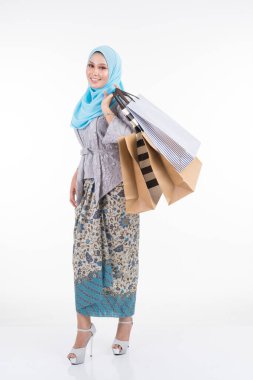 Geleneksel Asya elbisesi içinde güzel bir Müslüman kadın model modern kebaya ve beyaz arka planda izole edilmiş alışveriş torbaları taşıyan bir tesettür. Eidul Fitri moda ve festival alışveriş konsepti