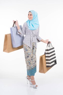 Geleneksel Asya elbisesi içinde güzel bir Müslüman kadın model modern kebaya ve beyaz arka planda izole edilmiş alışveriş torbaları taşıyan bir tesettür. Eidul Fitri moda ve festival alışveriş konsepti