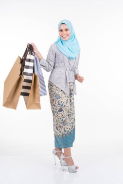 Geleneksel Asya elbisesi içinde güzel bir Müslüman kadın model modern kebaya ve beyaz arka planda izole edilmiş alışveriş torbaları taşıyan bir tesettür. Eidul Fitri moda ve festival alışveriş konsepti