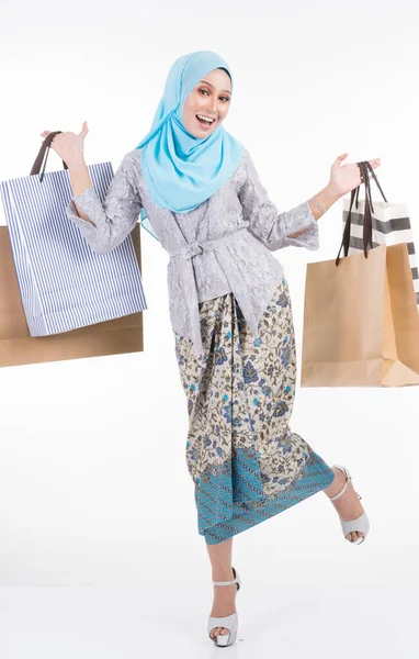 Geleneksel Asya elbisesi içinde güzel bir Müslüman kadın model modern kebaya ve beyaz arka planda izole edilmiş alışveriş torbaları taşıyan bir tesettür. Eidul Fitri moda ve festival alışveriş konsepti