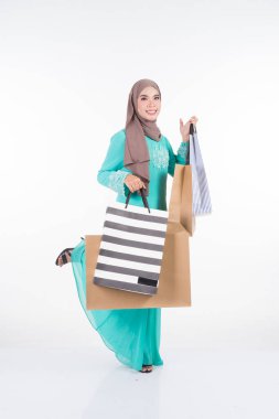 Geleneksel Asya elbisesi içinde güzel ve heyecanlı bir kadın model beyaz arka planda izole edilmiş alışveriş torbaları taşıyan modern bir kurung. Eidul Fitri festival hazırlık alışveriş konsepti. Tam boy portre.