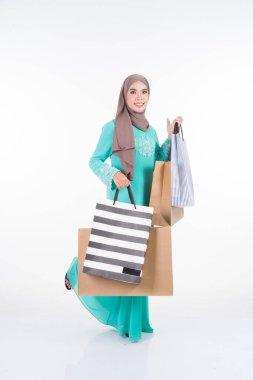 Geleneksel Asya elbisesi içinde güzel ve heyecanlı bir kadın model beyaz arka planda izole edilmiş alışveriş torbaları taşıyan modern bir kurung. Eidul Fitri festival hazırlık alışveriş konsepti. Tam boy portre.