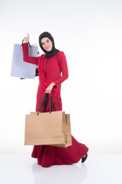 Beyaz arka planda izole edilmiş alışveriş torbaları taşıyan geleneksel kırmızı elbiseli güzel bir Asyalı kadın manken. Eidul Fitri festival alışveriş konsepti. Tam boy portre.