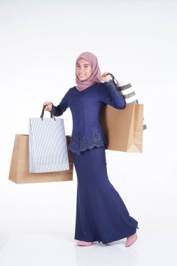 Geleneksel Asya elbisesi içinde güzel ve heyecanlı bir Müslüman kadın model beyaz arka planda izole edilmiş alışveriş torbaları taşıyor. Eidul Fitri moda ve festival hazırlık alışveriş konsepti
