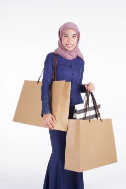 Geleneksel Asya elbisesi içinde güzel ve heyecanlı bir Müslüman kadın model beyaz arka planda izole edilmiş alışveriş torbaları taşıyor. Eidul Fitri moda ve festival hazırlık alışveriş konsepti