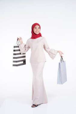 Geleneksel Asya elbisesi içinde güzel ve heyecanlı bir Müslüman kadın model beyaz arka planda izole edilmiş alışveriş torbaları taşıyor. Eidul Fitri moda ve festival hazırlık alışveriş konsepti