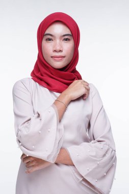 Beyaz arka planda izole edilmiş Asyalı Müslüman geleneksel bir elbise olan kırmızı tesettürlü, krem renkli modern kebaya giymiş güzel bir Müslüman kadın modelin yakın çekimi. Eidul Fitri moda ve yaşam tarzı portresi konsepti.