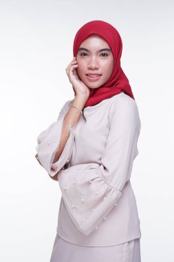 Beyaz arka planda izole edilmiş Asyalı Müslüman geleneksel bir elbise olan kırmızı tesettürlü, krem renkli modern kebaya giymiş güzel bir Müslüman kadın modelin yakın çekimi. Eidul Fitri moda ve yaşam tarzı portresi konsepti.