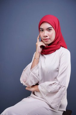 Gri arka planda izole edilmiş Asyalı Müslüman geleneksel bir elbise olan kırmızı tesettürlü, krem renkli modern kebaya giymiş güzel bir Müslüman kadın modelin yakın çekimi. Eidul Fitri moda ve yaşam tarzı portresi konsepti.