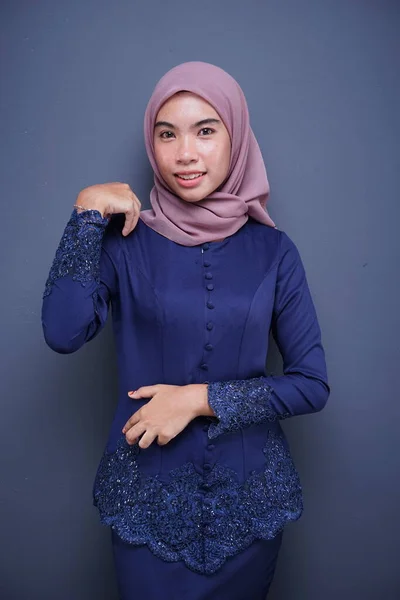 A beautiful Muslim female model wearing a dark blue modern kebaya with hijab, an Asian Muslim traditional dress isolated on grey background. Eidul fitri fashion and lifestyle portrait concept. Half portrait