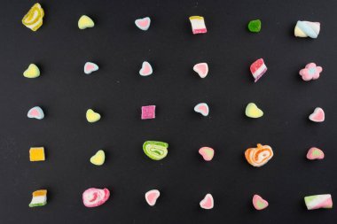 Esmer arka planda renkli şekerler ve tatlılar için yaratıcı bir düzen. Düz görünüm.