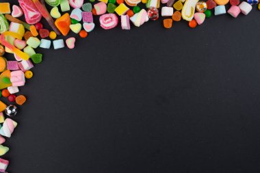Esmer arka planda renkli şekerler ve tatlılar için yaratıcı bir düzen. Düz görünüm.