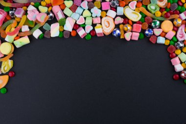 Esmer arka planda renkli şekerler ve tatlılar için yaratıcı bir düzen. Düz görünüm.