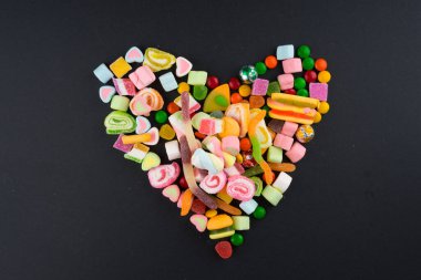 Esmer arka planda renkli şekerler ve tatlılar için yaratıcı bir düzen. Düz görünüm.