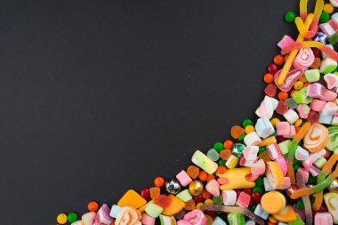 Esmer arka planda renkli şekerler ve tatlılar için yaratıcı bir düzen. Düz görünüm.