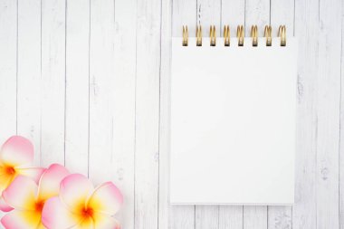 Frangipani çiçeklerinin yaratıcı düzenlemesi ve ahşap doku arka planında sarmal defter. Zen aromaterapi kavramı. Metin için dizüstü bilgisayara boşluk kopyala.