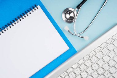 Tıbbi ya da sağlık hizmeti konsepti. Stetoskop ve mavi arka planda spiral not defteri gibi tıbbi cihazlar. Düz görünüm.
