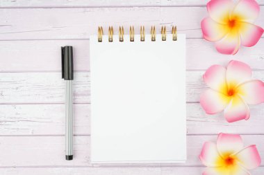 Frangipani çiçeklerinin yaratıcı düzenlemesi ve ahşap doku arka planında sarmal defter. Zen aromaterapi kavramı. Metin için dizüstü bilgisayara boşluk kopyala.