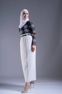 Güzel bir Müslüman kadın modelin, tesettürlü ve gri arka planda gündelik giyimli tam boy portresi. Başörtüsü ve Müslüman yaşam tarzı konsepti