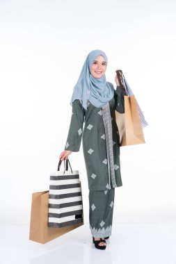 Geleneksel Asya elbisesi içinde güzel ve heyecanlı bir Müslüman kadın model beyaz arka planda izole edilmiş alışveriş torbaları taşıyor. Eidul Fitri moda ve festival hazırlık alışveriş konsepti