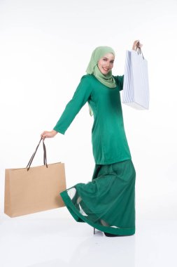 Modern bir kurungda beyaz arka planda izole edilmiş alışveriş torbaları taşıyan güzel bir Asyalı kadın model. Eidul Fitri festival hazırlık alışveriş konsepti. Tam boy portre.
