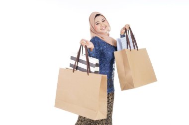 Geleneksel Asya elbisesi içinde güzel ve heyecanlı bir kadın model beyaz arka planda izole edilmiş alışveriş torbaları taşıyan modern bir kurung. Eidul Fitri moda ve festival hazırlık alışveriş konsepti.