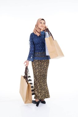 Geleneksel Asya elbisesi içinde güzel ve heyecanlı bir kadın model beyaz arka planda izole edilmiş alışveriş torbaları taşıyan modern bir kurung. Eidul Fitri moda ve festival hazırlık alışveriş konsepti