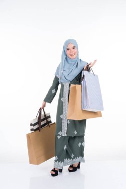 Geleneksel Asya elbisesi içinde güzel ve heyecanlı bir Müslüman kadın model beyaz arka planda izole edilmiş alışveriş torbaları taşıyor. Eidul Fitri moda ve festival hazırlık alışveriş konsepti