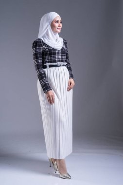 Güzel bir Müslüman kadın modelin, tesettürlü ve gri arka planda gündelik giyimli tam boy portresi. Başörtüsü ve Müslüman yaşam tarzı konsepti