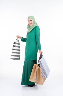 Modern bir kurungda beyaz arka planda izole edilmiş alışveriş torbaları taşıyan güzel bir Asyalı kadın model. Eidul Fitri festival hazırlık alışveriş konsepti. Tam boy portre.