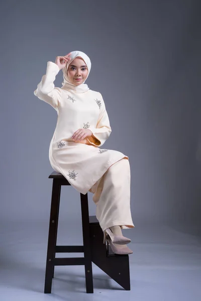 Beautiful female Muslim model wearing kurung Pahang and hijab, an urban lifestyle apparel for Muslim women on grey. Beauty and hijab fashion concept. Full length portrait