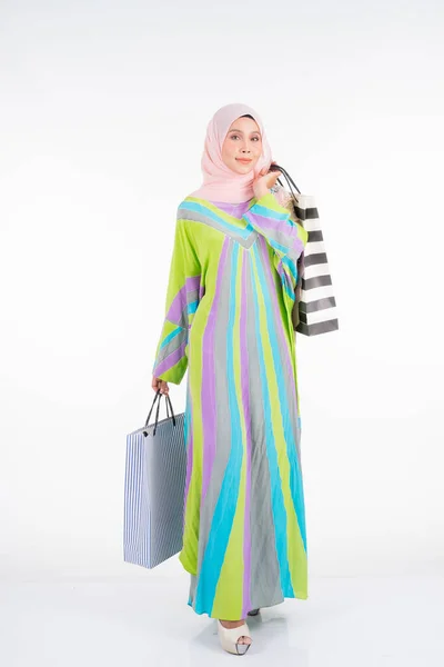 白を基調としたショッピングバッグを背景に 伝統的なカフタン カフタンのドレスを身に着けた美しく幸せなムスリム女性モデル Eidul Fitriファッションとお祝いの準備ショッピングコンセプト — ストック写真
