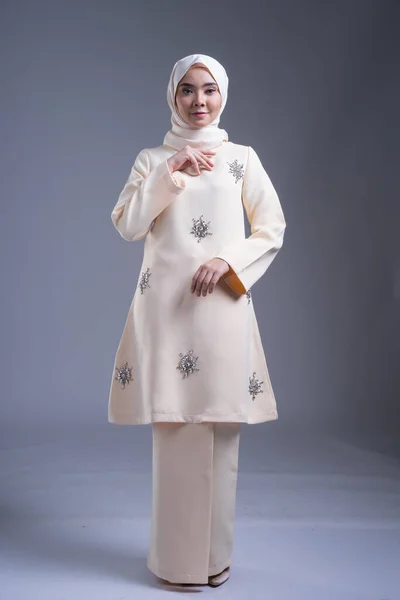 Beautiful female Muslim model wearing kurung Pahang and hijab, an urban lifestyle apparel for Muslim women on grey. Beauty and hijab fashion concept. Full length portrait