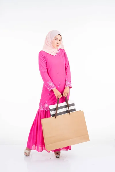 白を基調としたショッピングバッグを背景に伝統的なピンクのモダンなクルンで美しく興奮したイスラム教徒の女性モデル Eidul Fitriファッションとお祝いのショッピングコンセプト — ストック写真