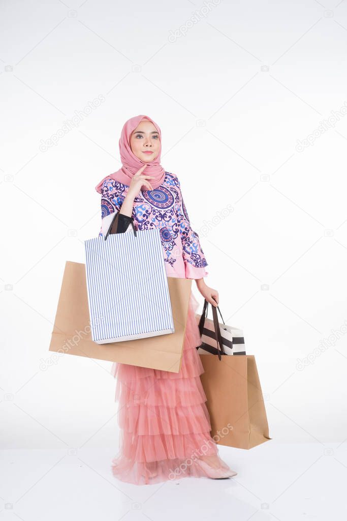 A beautiful Muslim female model in a Asian traditional dress carrying shopping bags isolated on white background. Eidul fitri festive preparation shopping concept. Full length portrait.