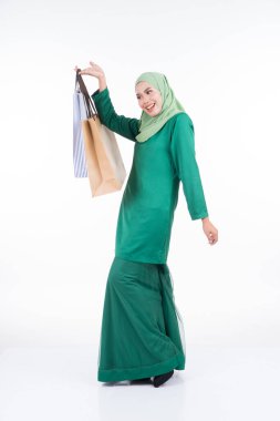 Modern bir kurungda beyaz arka planda izole edilmiş alışveriş torbaları taşıyan güzel bir Asyalı kadın model. Eidul Fitri festival hazırlık alışveriş konsepti. Tam boy portre.