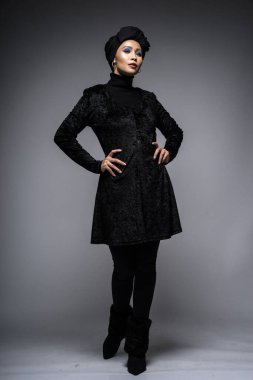 Siyah bluzlu ve gri arka planda türbanı olan Asyalı bir kadının yüksek moda portresi. Başörtüsü modası için moda editörlüğü konsepti. Tam uzunluk