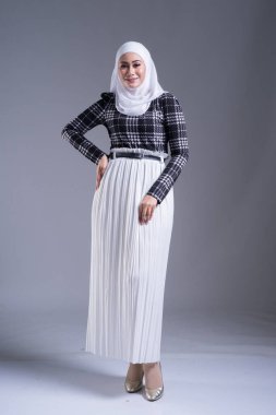 Güzel bir Müslüman kadın modelin, tesettürlü ve gri arka planda gündelik giyimli tam boy portresi. Başörtüsü ve Müslüman yaşam tarzı konsepti