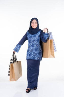 Geleneksel Asya elbisesi içinde güzel ve heyecanlı bir kadın model beyaz arka planda izole edilmiş alışveriş torbaları taşıyan modern bir kurung. Eidul Fitri moda ve festival hazırlık alışveriş konsepti