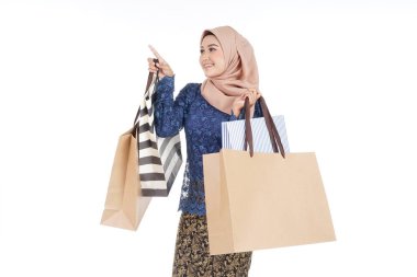 Geleneksel Asya elbisesi içinde güzel ve heyecanlı bir kadın model beyaz arka planda izole edilmiş alışveriş torbaları taşıyan modern bir kurung. Eidul Fitri moda ve festival hazırlık alışveriş konsepti.