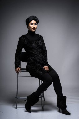 Siyah bluzlu ve gri arka planda türbanı olan Asyalı bir kadının yüksek moda portresi. Başörtüsü modası için moda editörlüğü konsepti. Tam uzunluk