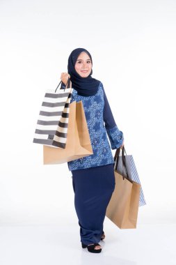 Geleneksel Asya elbisesi içinde güzel ve heyecanlı bir kadın model beyaz arka planda izole edilmiş alışveriş torbaları taşıyan modern bir kurung. Eidul Fitri moda ve festival hazırlık alışveriş konsepti