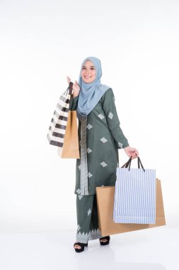Geleneksel Asya elbisesi içinde güzel ve heyecanlı bir Müslüman kadın model beyaz arka planda izole edilmiş alışveriş torbaları taşıyor. Eidul Fitri moda ve festival hazırlık alışveriş konsepti