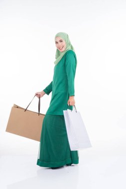 Modern bir kurungda beyaz arka planda izole edilmiş alışveriş torbaları taşıyan güzel bir Asyalı kadın model. Eidul Fitri festival hazırlık alışveriş konsepti. Tam boy portre.